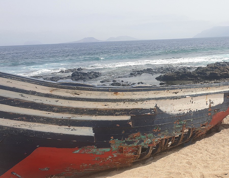 Restos de una embarcación utilizada en una travesía migratoria, varada en una playa del norte de Lanzarote, con La Graciosa al fondo / Foto: Archivo Elpejeverde.com